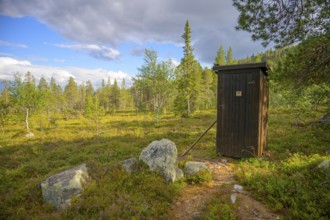 Wooden cabin in forest surrounded by trees and mossy ground under cloudy sky, Gutulia National