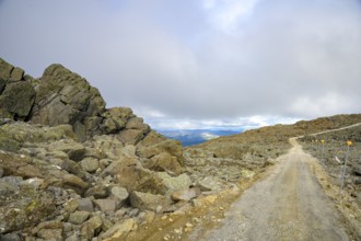 Alvdal, Innlandet, Norway, Rocky road leads through a barren mountain landscape under cloudy sky,