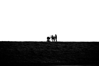 Silhouette of family walking with stroller on grassy dike at Jade Bay, Wadden Sea National Park,