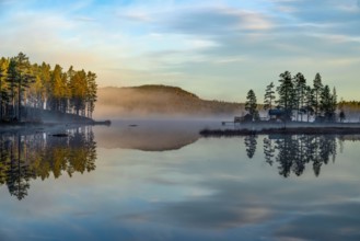 Calm lake with trees and hills in morning fog, picturesque and peaceful atmosphere