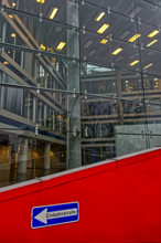 A modern glass building reflects the surrounding area, while a red sign shows the entrance