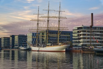 Historic sailing ship in a quiet harbor in front of modern houses