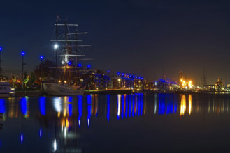 Nocturnal harbor with illuminated sailing ship and reflections in calm water