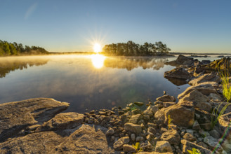 Sunrise over a quiet lake with rocks in the foreground and clear air