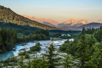 A river snakes through a wooded landscape with mountains at sunset