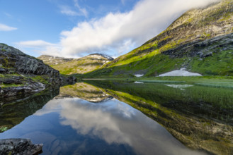 Mountains with snow-capped peaks reflected in clear water surrounded by green vegetation