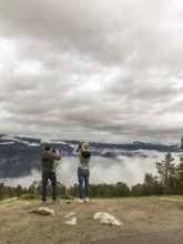 Utvik, Vestland, Norway, Two people photograph a foggy landscape with mountains and clouds with