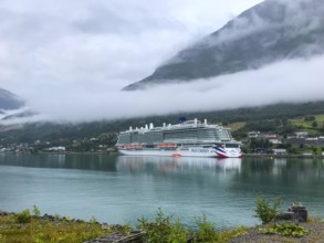 Olden, Vestland, Norway, Large cruise ship anchors in a fjord with forested mountains and clouds of
