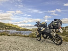 Haugastøl, Viken, Norway, A loaded motorcycle on a road with lake and mountain views in the