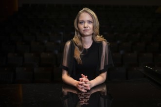 Young woman, pianist, in evening dress, with folded hands supported on Steinway & Sons grand piano,