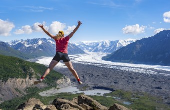 Young woman jumping into the air, view of impressive mountain landscape with Matanuska glacier and