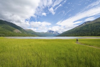 Young man in a green meadow by a lake, Eklutna Lake, Chugach Mountains, Chugach State Park, Alaska,
