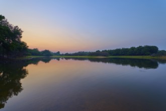 Gentle twilight to a calm lake, with trees on the horizon and blue sky, Fazenda Barranco Alto, Rio