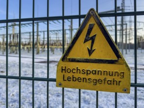 Recording of snow in winter warning sign warning high voltage danger to life on fence from behind