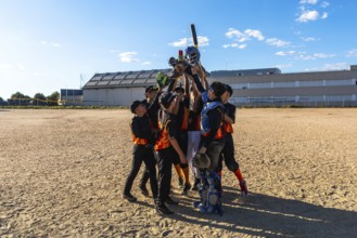 Young baseball players huddling together with arms raised in victory, holding bats, gloves, and