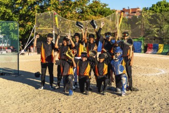 Young baseball team and coach standing together on an outdoor dirt field, raising bats and gloves