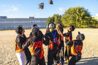 Young baseball players with gloves and uniforms celebrating a game victory together on a dirt