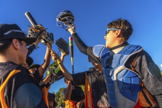 Young baseball team members cheering together, raising bats, gloves, and a catcher's helmet into
