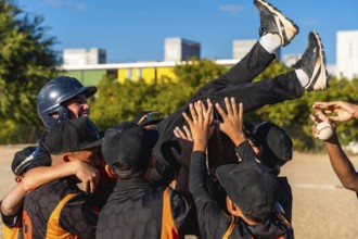 Young baseball teammates lift a smiling boy in celebration after a game, sharing joyful camaraderie