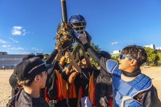 Baseball players huddling together, raising their catcher's helmet, bat, and gloves in the air,