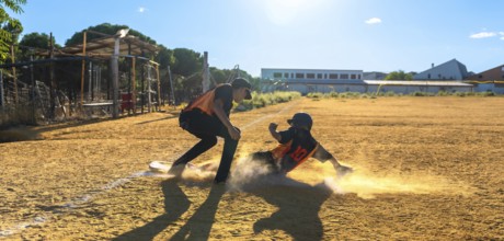 Two baseball players on a sunny field, one slides into a dusty base in a cloud of dirt while