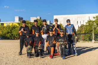Young baseball players wearing uniforms and protective gear on a sunny day, standing and kneeling