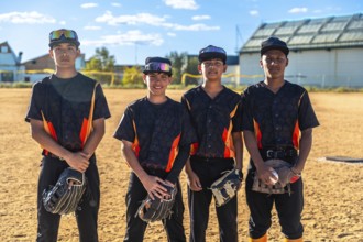 Young baseball teammates in uniforms posing with mitts and a ball on a dusty sunlit field, ready