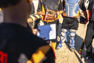 Coach holding clipboard with baseball field diagram, explaining plays and strategy to youth team