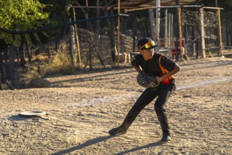 Young boy in cap and sunglasses poised to catch a baseball with his glove on a sunny dirt field