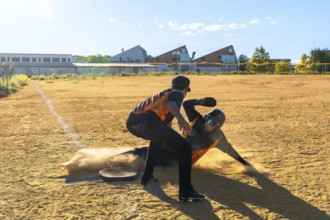 Baseball player sliding into the base with dust kicking up while an opponent stands by, capturing