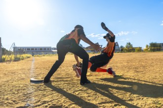 Two young baseball players are competing on a dusty field. With one player sliding dramatically