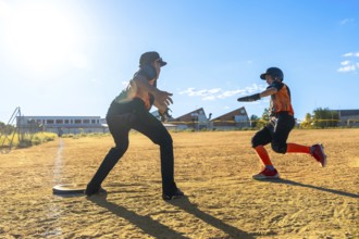 Youth baseball player sprinting hard across the dirt toward a base while coach or teammate awaits,