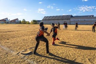Young baseball players competing in a game on a sunny day, with one player sliding into second base