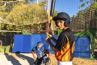 Young baseball batter wearing a helmet and looking at the camera while holding a bat, with a