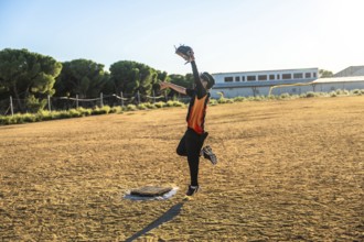 Young baseball player in uniform and glove jumping to catch a flying ball on a sunny dirt field,