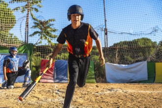 Young male baseball player running on a dirt field during a game or practice, wearing a helmet and