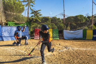 Kids playing baseball on a sunny day, an unidentifiable male batter wearing a helmet and looking