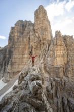 Mountaineer stretches his arms in the air, climbs an exposed rock in the secured Via Ferrata