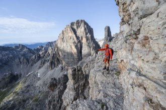 Mountaineer points into the distance, climbs an exposed rock band in the secured Via Ferrata