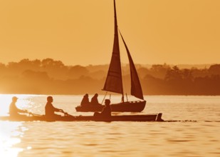 Boats on a lake at sunset with people in a quiet evening mood in the foreground a roundboat with