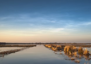 Extensive landscape with blue skies and delicate clouds is reflected in the water, soft yellow