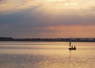 Two children 6 and 10 years old in a small red sailboat Optimist Jolle Opti on the Dümmer at golden