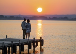 A couple stands on a jetty and looks at a colorful sunset over Lake Dümmer, Lembruch, Dümmer nature