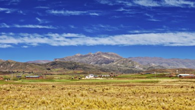 Wide fields in front of a mountain range under a cloudy sky, The Altiplano landscape in the Andes