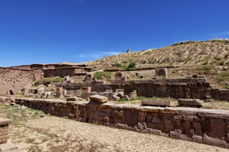 Ancient stone ruin structure against a clear blue sky surrounded by barren landscape and hills, the