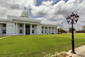 A white building with dome and pillars surrounded by green lawn under cloudy sky, Colombo Sri Lanka