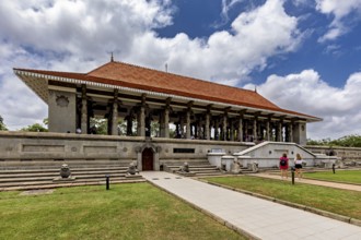 A long building with pillars and a distinctive roof surrounded by lawns on a cloudy day, Colombo