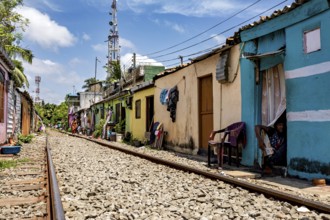 Tracks lead through residential area with bright houses and chairs outside under sunny skies,