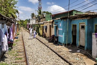 Narrow street along railroad tracks flanked by colorful houses under clear skies, railway line in