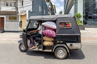 A loaded car rickshaw drives through an urban environment in sunny weather, tuk tuk transport in